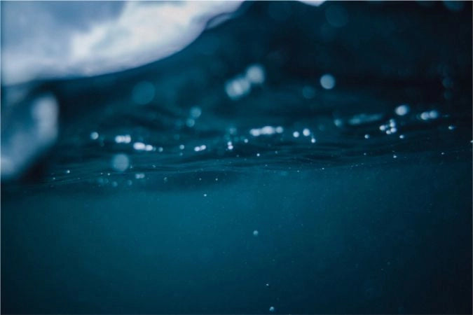 Underwater view with the surface of the water above and small bubbles scattered throughout the cool, dark blue depths.