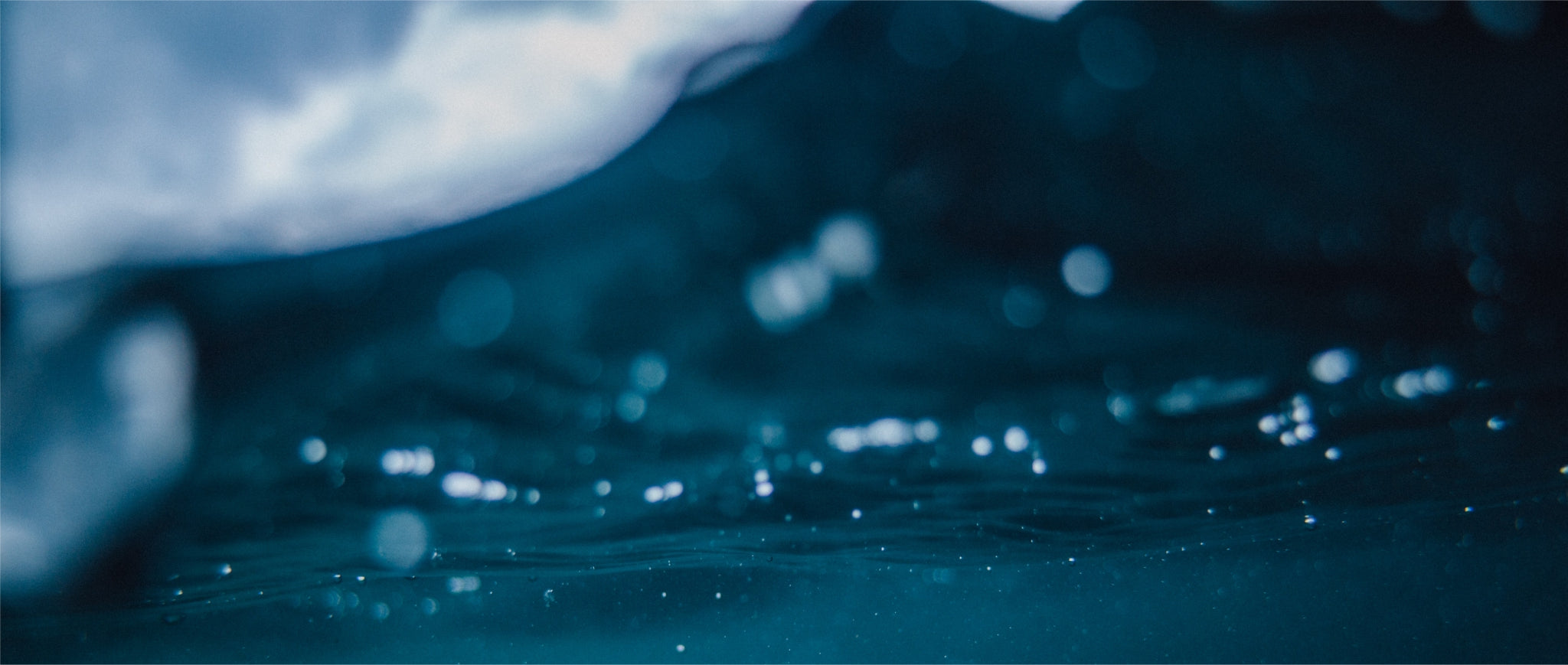 Underwater view with the surface of the water above and small bubbles scattered throughout the cool, dark blue depths.