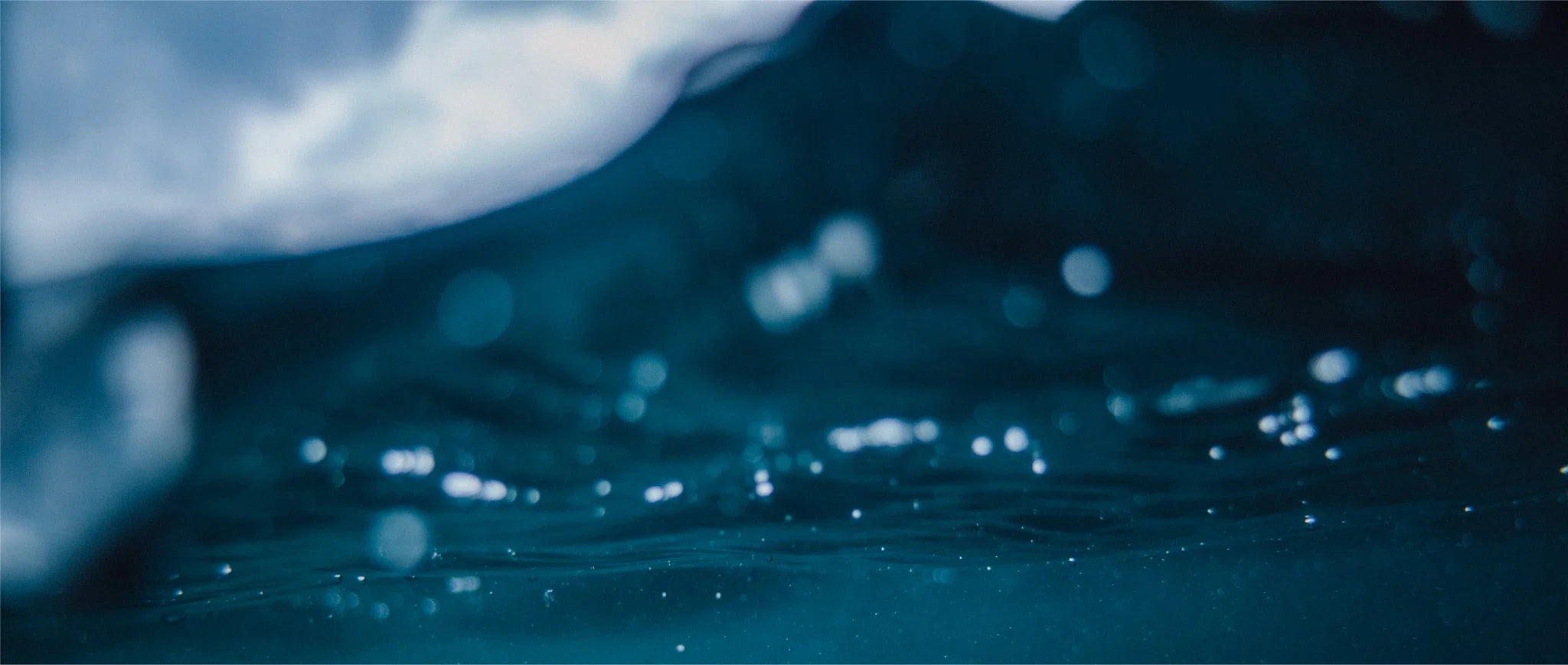 Underwater view with the surface of the water above and small bubbles scattered throughout the cool, dark blue depths.