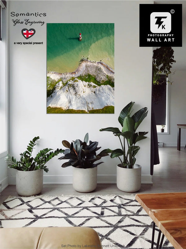 Living room with a large wall art print of Beach Head Cliff and Lighthouse, surrounded by potted plants.