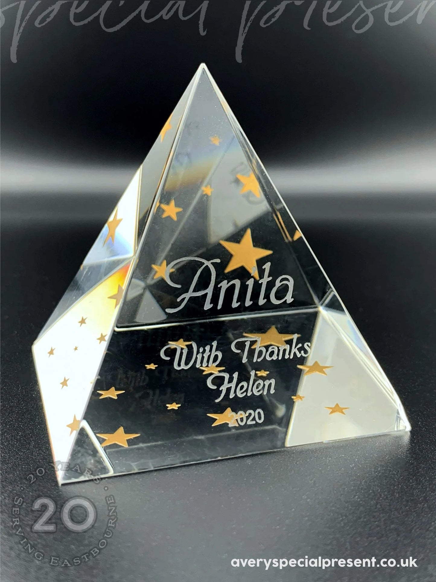 This is a Pyramid crystal gift with a glossy finish, standing upright. The award features a bold, personalized engraving with the name "Anita" prominently centered in a large, elegant font. Below, in a smaller but equally sophisticated script, reads "With Thanks, Helen 2020," surrounded by a constellation of finely etched golden stars, adding a celebratory flair to the piece. The website "averyspecialpresent.co.uk" subtly suggests its origin, completing this bespoke memento that reflects light beautifully.