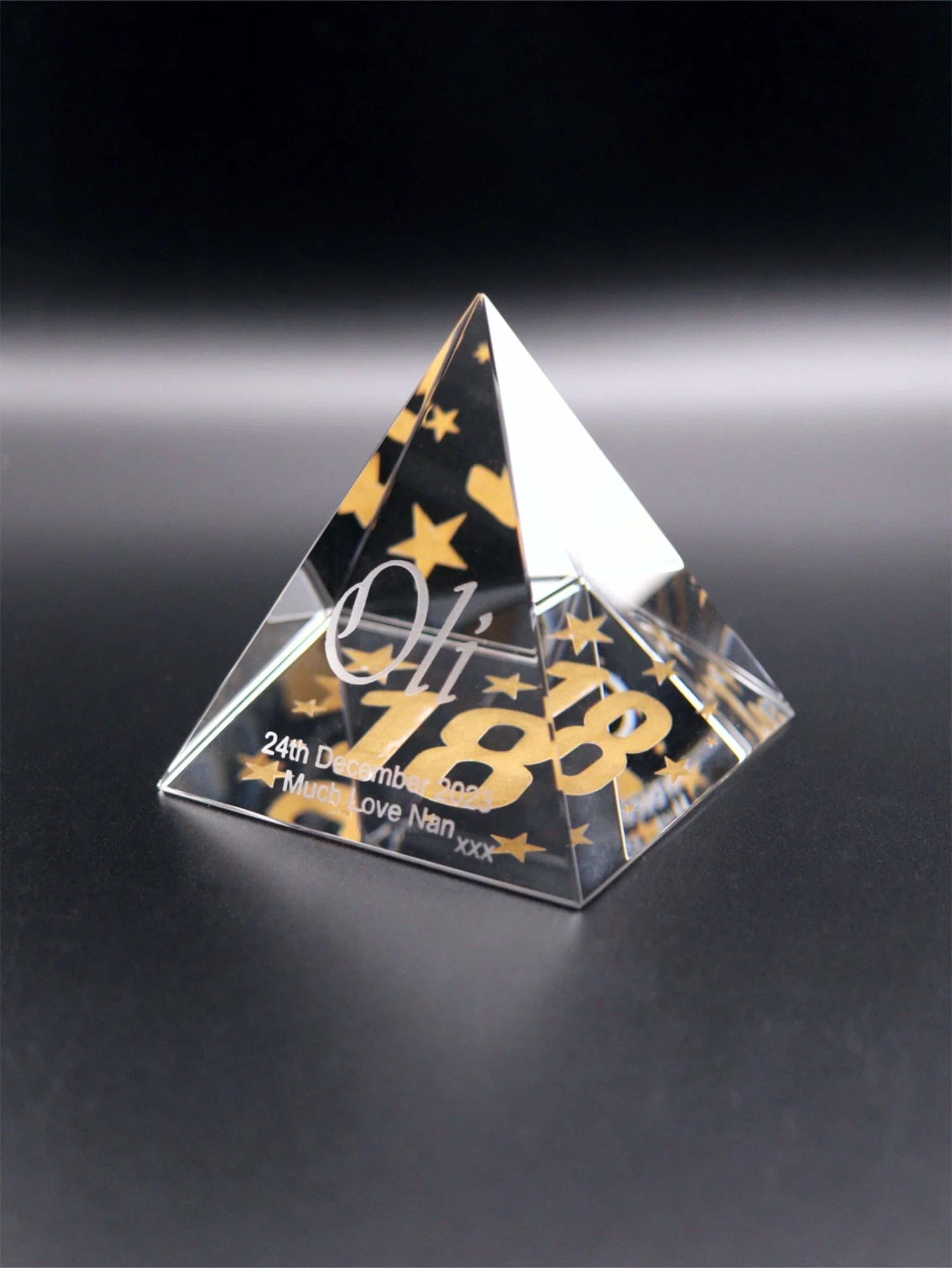 A square based pyramid, engraved on the base and inlaid with gold enamelling, stars surrounding a large 18. Engraved on the face is Oli, the date, Much Love Nan xxx.