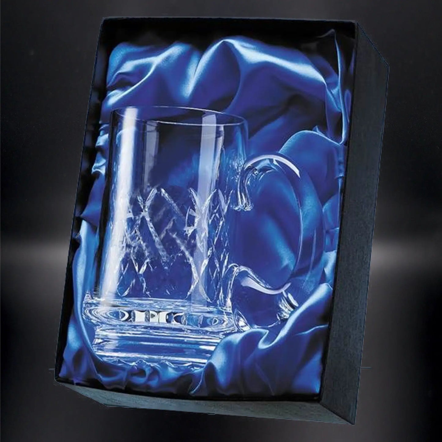 A crystal whiskey glass with a robust base and intricate diamond-cut pattern, nestled in a luxurious blue satin-lined presentation box. The glass's clarity and craftsmanship are highlighted against the rich fabric, making it a sophisticated gift choice.